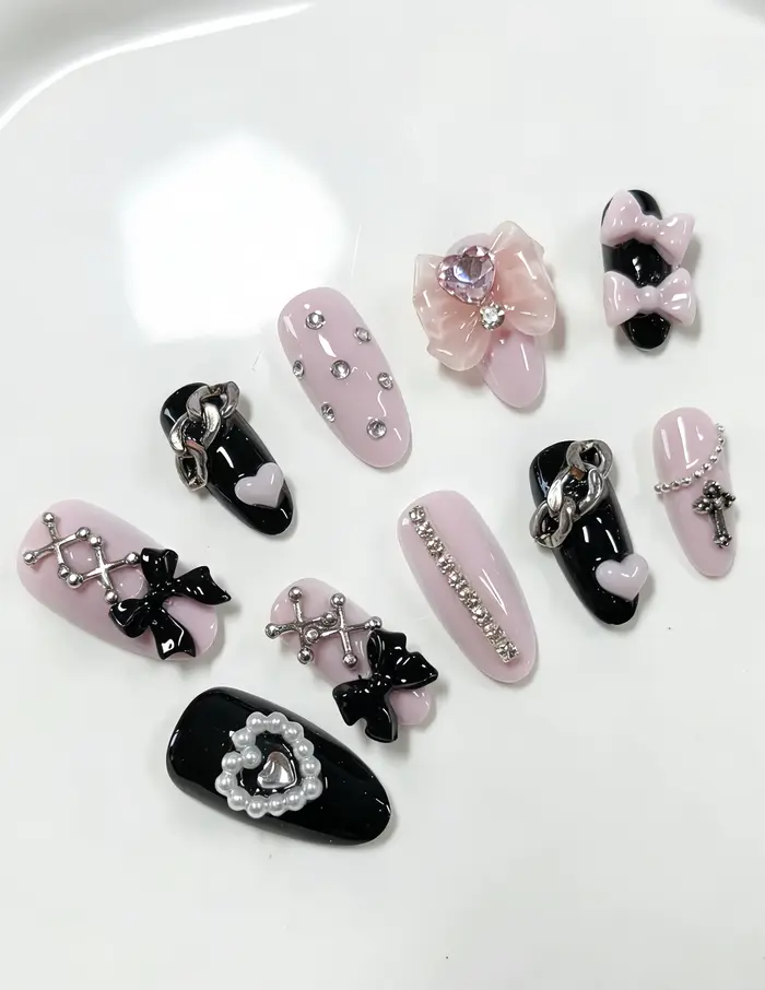 10 ongles en forme d'amande, aux couleurs principales rose et noir, décorés de nœuds 3D, de strass e